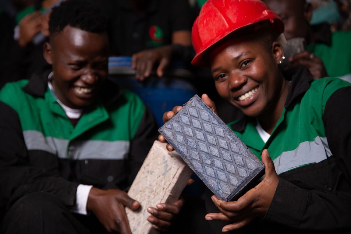 Two smiling Gjenge team members holding recycled plastic bricks
